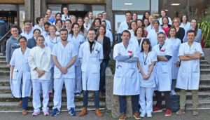 Group of medical professionals and staff, wearing white lab coats, standing on outdoor steps in front of a building.