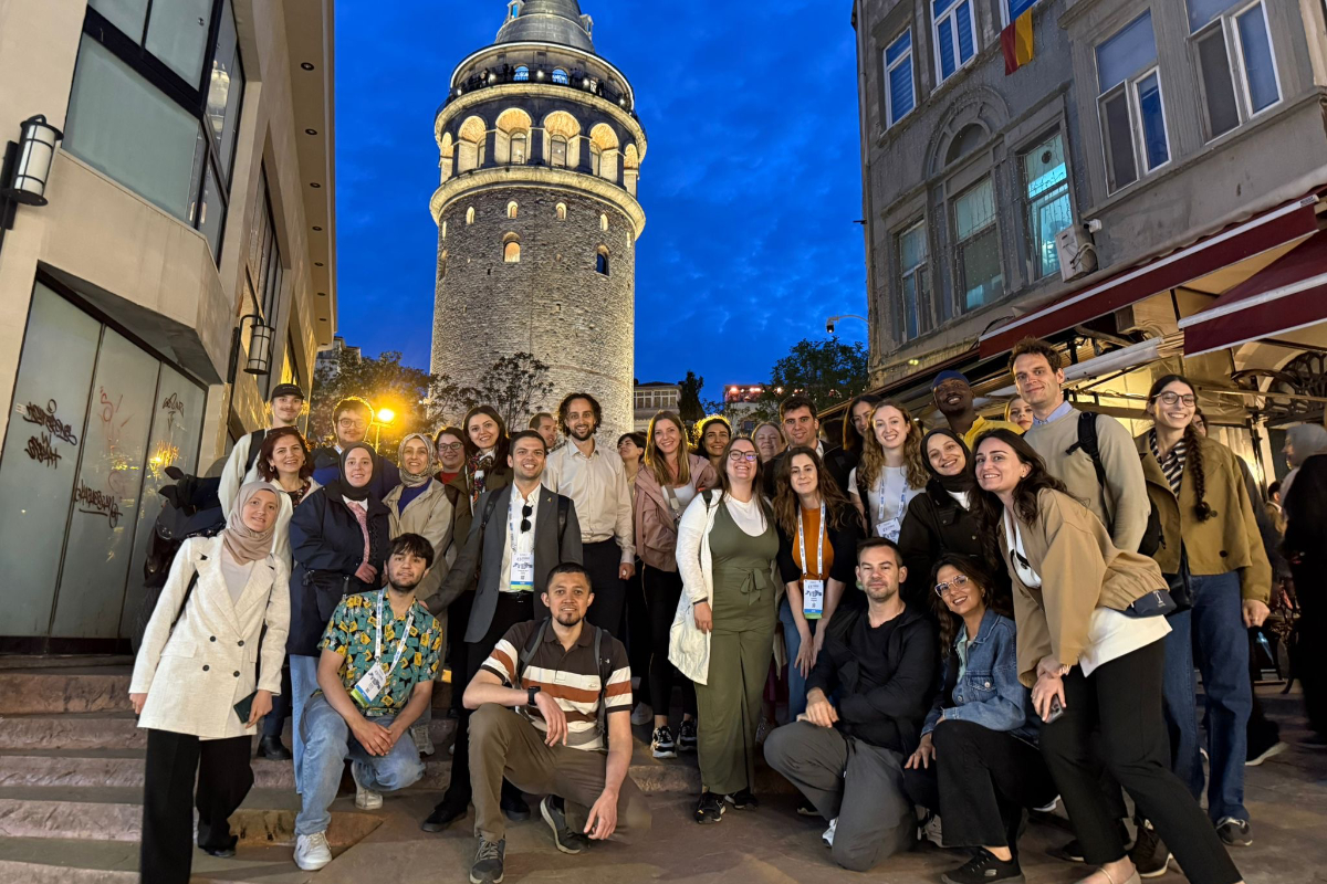 A group of people pose for a photo at night in front of the illuminated Galata Tower, surrounded by city buildings.