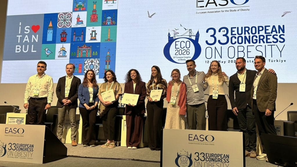 A group of people poses onstage with certificates at the 33rd European Congress on Obesity in Istanbul, with event banners and a city-themed backdrop behind them.