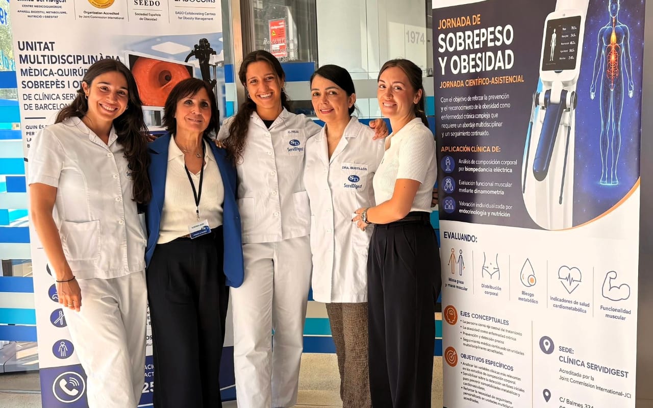 Five women, four in medical uniforms and one in business attire, stand smiling in front of banners about obesity and multidisciplinary medical care.