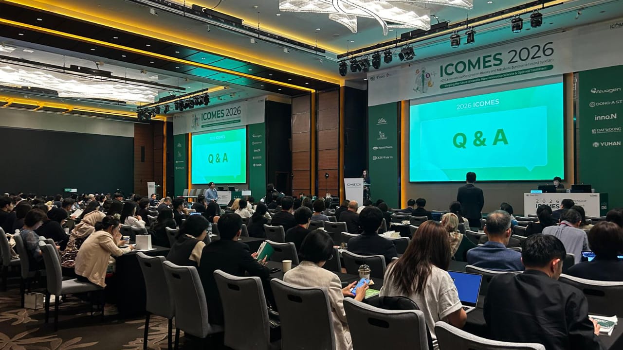 A conference room filled with seated attendees faces a stage with large screens displaying “Q & A” and “ICOME 2026” banners.